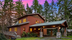 A two-story log cabin with a stone foundation, a covered porch, and a wooden deck. - Enchanting Lindal Waterfront Cabin (Shelton)