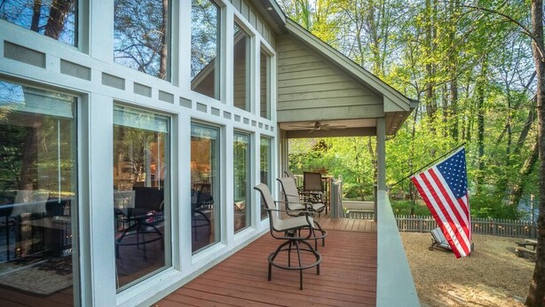 A covered deck with outdoor seating and a flag. - Luxury Riverfront Retreat | Hot Tub | Walk to Town (Helen)