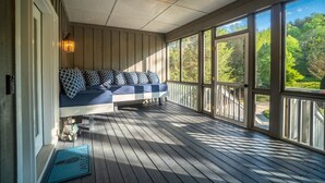 A covered porch with a built-in bench, large windows, and a view of the outdoors. - Luxury Riverfront Retreat | Hot Tub | Walk to Town (Helen)
