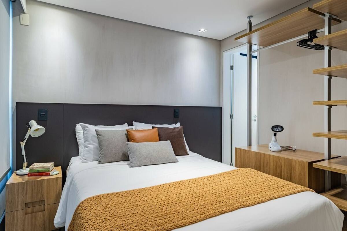 Una habitación de hotel moderna con una cama grande, una mesita de noche con lámpara y un escritorio de madera con silla.