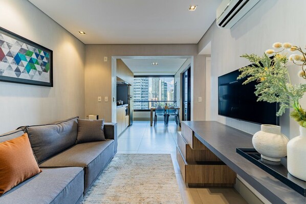 A modern living room with a sofa, a TV, and a dining area in the background.