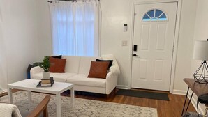 A living room with a white sofa, a small table, a potted plant, and a door with a window. - Pet Friendly, Extended Stay 30+ (Johnson City)