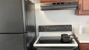 A kitchen with wooden cabinets, a black refrigerator, and a white stove with pots. - Pet Friendly, Extended Stay 30+ (Johnson City)