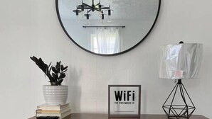 A round mirror on a wall, a small table with a potted plant, a framed sign, and two woven baskets. - Pet Friendly, Extended Stay 30+ (Johnson City)