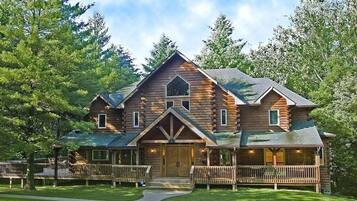 A log cabin with a central entrance, a porch, and a fenced yard.