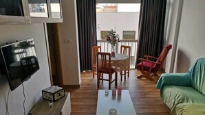 A living room with a TV, a coffee table, a sofa, a dining table with chairs, and a balcony view. - Amplio, Luminoso y Confortable; 15 Minutos del Centro (Málaga)