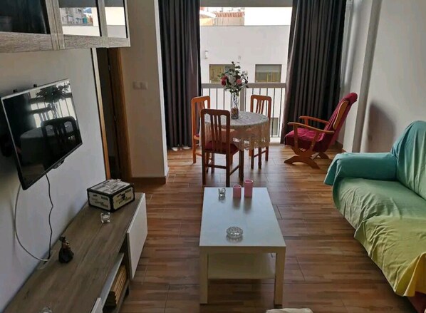 Un salon équipé d’un téléviseur, d’une table basse, d’un canapé, d’une table à manger avec des chaises et offrant une vue sur le balcon.