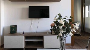 A modern living room with a flat-screen TV mounted on the wall, a wooden cabinet with glass doors, and a vase with flowers on a table. - Amplio, Luminoso y Confortable; 15 Minutos del Centro (Málaga)