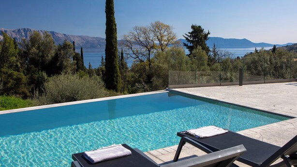 A rectangular swimming pool with clear blue water, surrounded by lounge chairs and a view of mountains and trees. - BITTER ALMOND TREES VILLAS - Stylish villa, sea views 1000m from Nikiana & Beach (Lefkada)