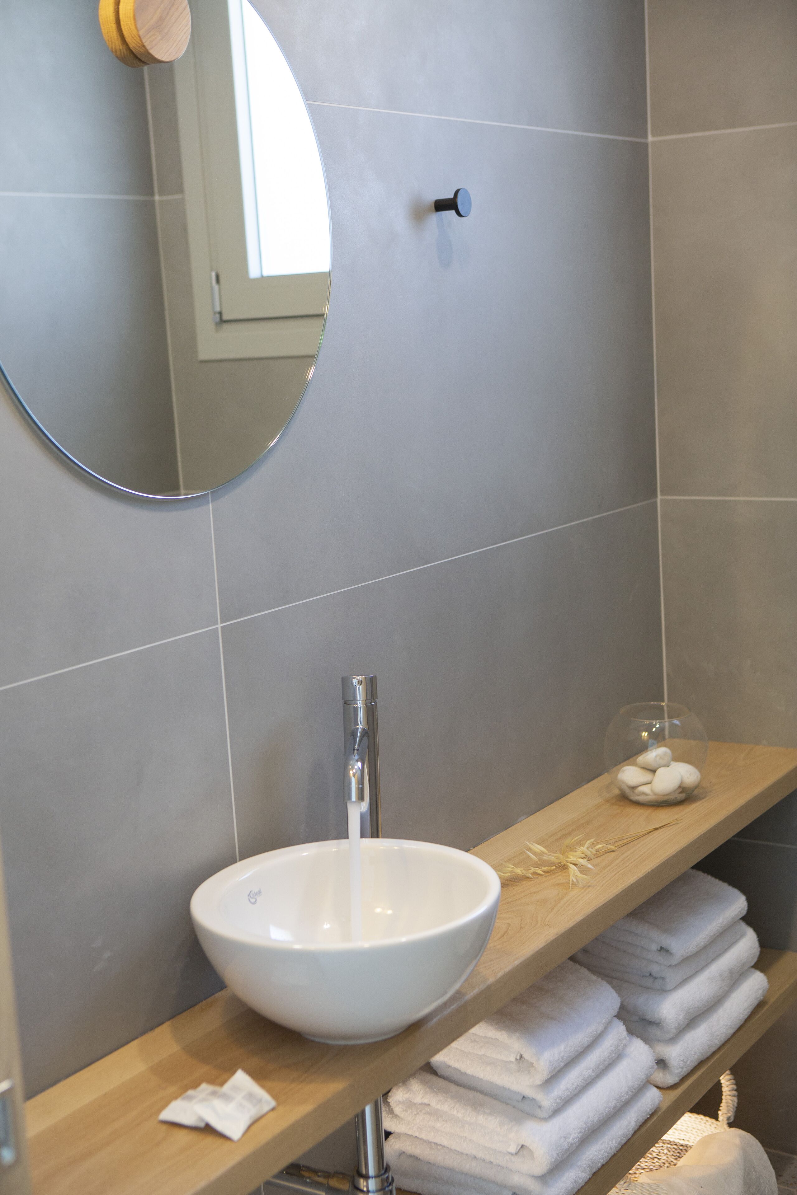 A bathroom with a white sink, a mirror, and a shelf with towels.