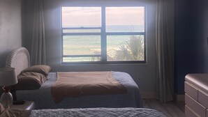 Ein Schlafzimmer mit einem großen Fenster mit Meerblick, einem Bett mit gestreifter Bettdecke und einem Schminktisch.
