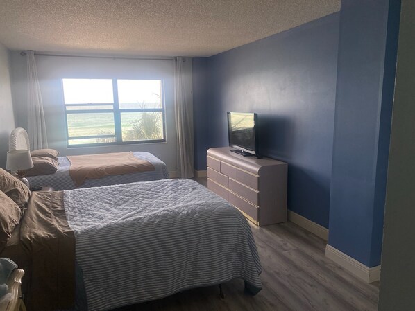 A bedroom with two beds, a dresser, a television, and a window with a view of the outdoors.