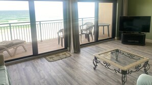 Ein Zimmer mit Balkon, Fernseher, Tisch und Sofa.