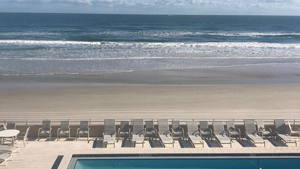 Blick auf einen Strand mit einem Poolbereich, ausgestattet mit Liegestühlen und einem Tisch.