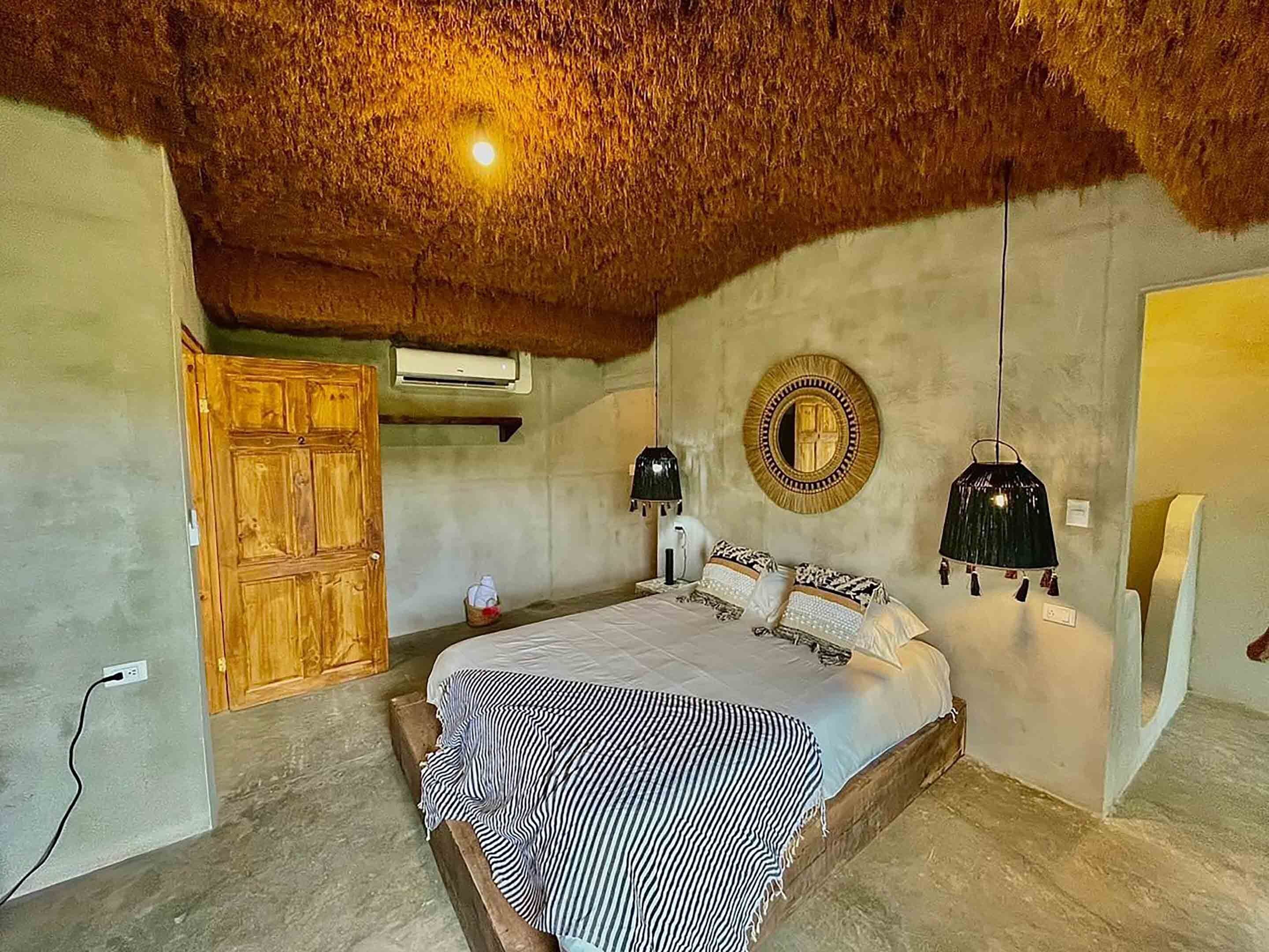 Een slaapkamer met een bed, een houten garderobe, een spiegel en een hanglamp.