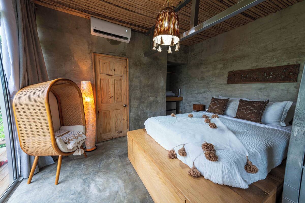 A bedroom with a bed, a chair, a hanging light fixture, and a wardrobe.