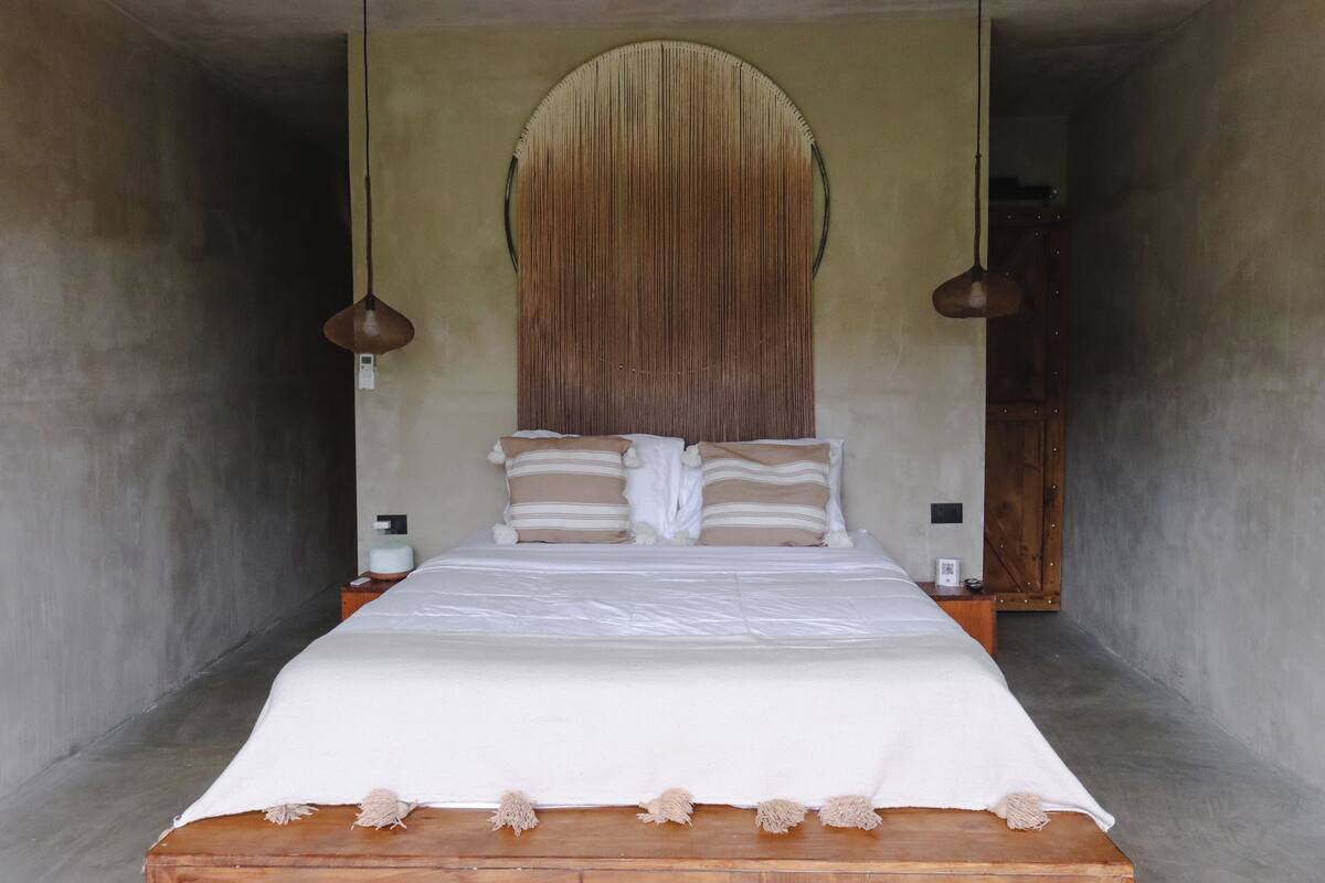 A bed with a white mattress and two pillows, a wooden headboard, and two pendant lights.