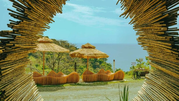 Uitzicht op een strand met rieten parasols en bamboe zitplaatsen.