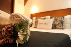 A neatly made bed with a folded towel and a floral arrangement beside it.
