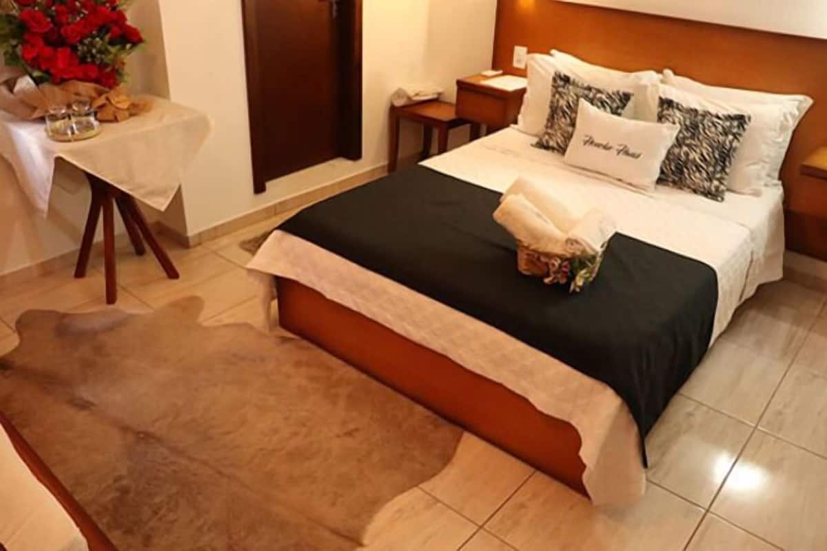 Ein Hotelzimmer mit einem Bett, einem Nachttisch, einem Tisch mit Blumen und einer Holztür.