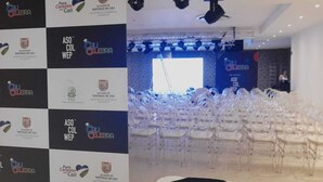 A conference room with rows of clear plastic chairs, a stage with lighting equipment, and banners with logos and text. - Hotel Qatar Cali (Cali)
