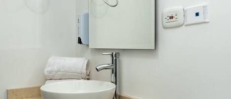 Un baño moderno con un lavamanos blanco, armarios oscuros y un espejo grande.