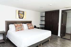Ein modernes Schlafzimmer mit einem großen Bett, zwei Zierkissen, einem Nachttisch, einem Kleiderschrank und einem Wandbild.