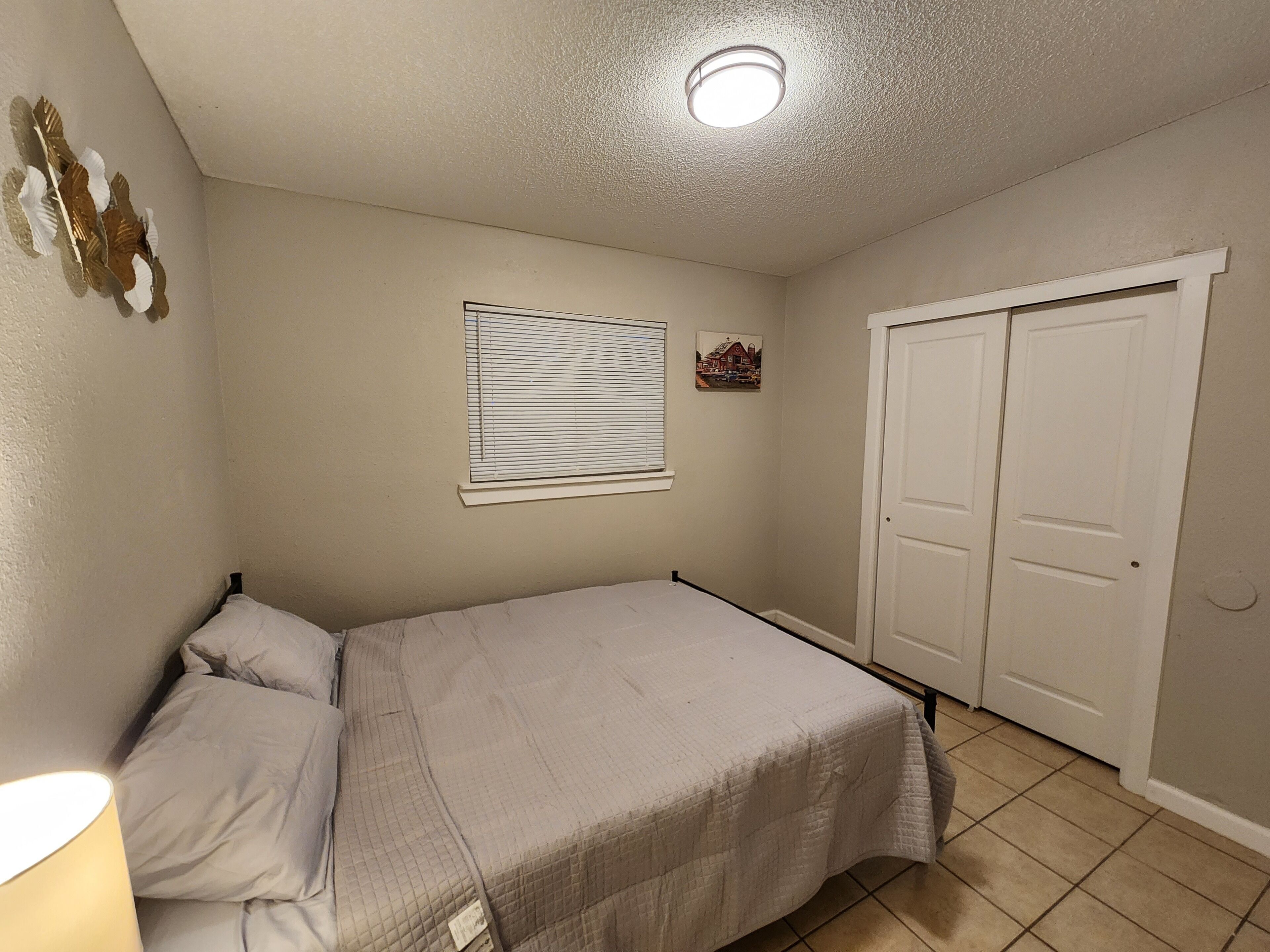 A bedroom with a bed, a window with blinds, a door, and a ceiling light.