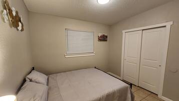A bedroom with a bed, a window with blinds, a door, and a ceiling light.