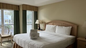Quarto de hotel com uma cama grande, uma cadeira, uma mesinha de cabeceira e uma janela com cortinas.