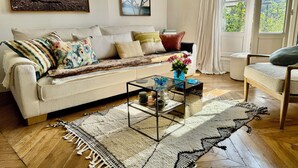 A cozy living room with a sofa, coffee table, and a view of greenery outside. - CENTRE MARAIS (picasso place des vosges) .A/C, WIFI, ELEVATOR, VUE, BALCONY ! (paris)