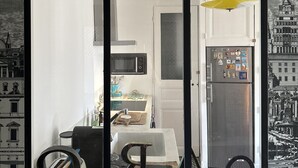 A modern kitchen with a refrigerator, microwave, and a hanging yellow light fixture. - CENTRE MARAIS (picasso place des vosges) .A/C, WIFI, ELEVATOR, VUE, BALCONY ! (paris)