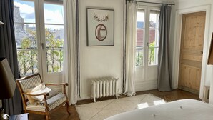 A bedroom with a large bed, a wooden chair, a radiator, and a view of the outside. - CENTRE MARAIS (picasso place des vosges) .A/C, WIFI, ELEVATOR, VUE, BALCONY ! (paris)