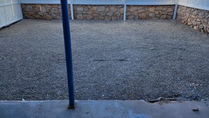 Un'area esterna recintata con fondo in ghiaia, muri in pietra e un palo in metallo.