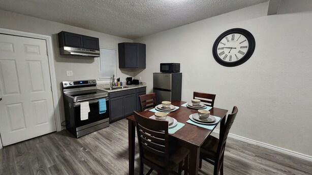 A compact kitchen with a dining area, including a stove, oven, microwave, and a clock on the wall.