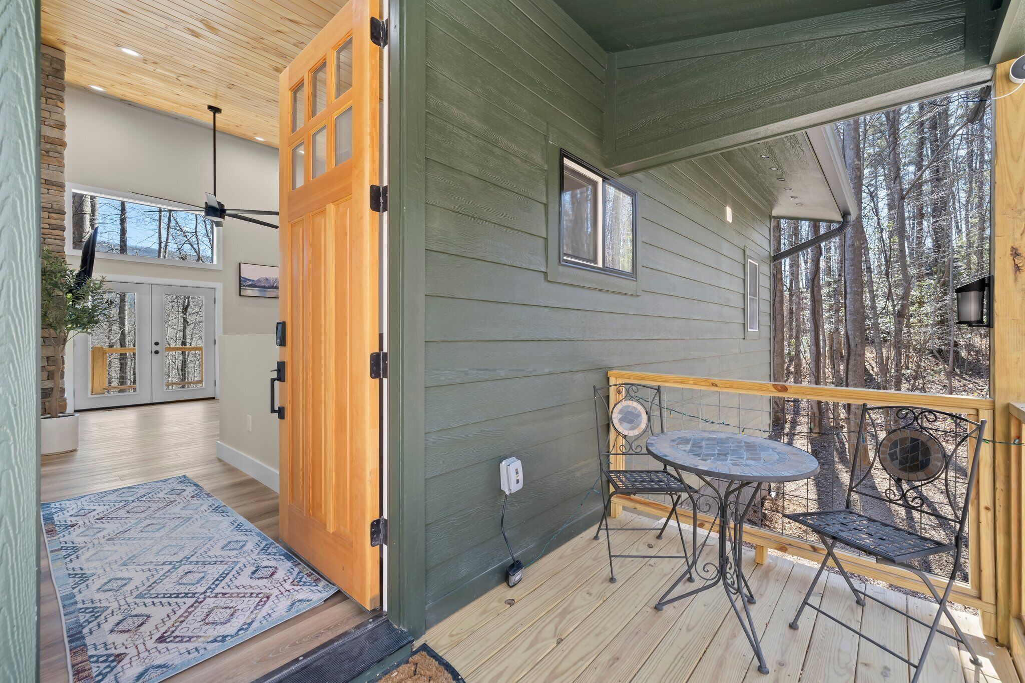 A wooden deck with a table and chairs, a view of trees, and a door leading to a room.