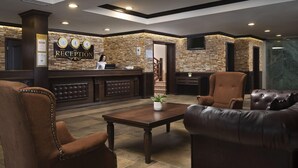 A reception area with a stone wall, a reception desk, leather chairs, a coffee table, and a television. - Apartment B25, Bansko, Royalpark (Bansko)
