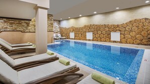 A swimming pool with lounge chairs and towels, surrounded by stone walls and wooden logs. - Apartment B25, Bansko, Royalpark (Bansko)