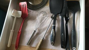 En kökslåda med olika köksredskap, inklusive en röd stekspade, en visp, en svart stekspade och en svart stekspade med ett hål.