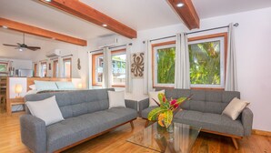 Una sala de estar moderna con dos sofás grises, una mesa de centro de cristal, suelo de madera y ventanas grandes con cortinas.