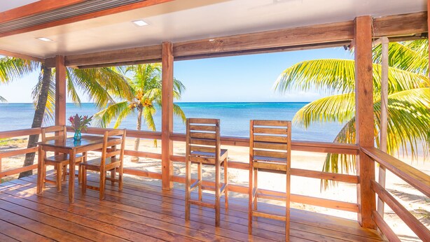 Una terraza de madera con sillas con vista a una playa con palmeras y el océano.