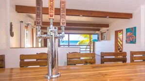 Un bar con varias griferías identificadas con nombres de cerveza, mobiliario de madera y vista al océano a través de amplios ventanales.