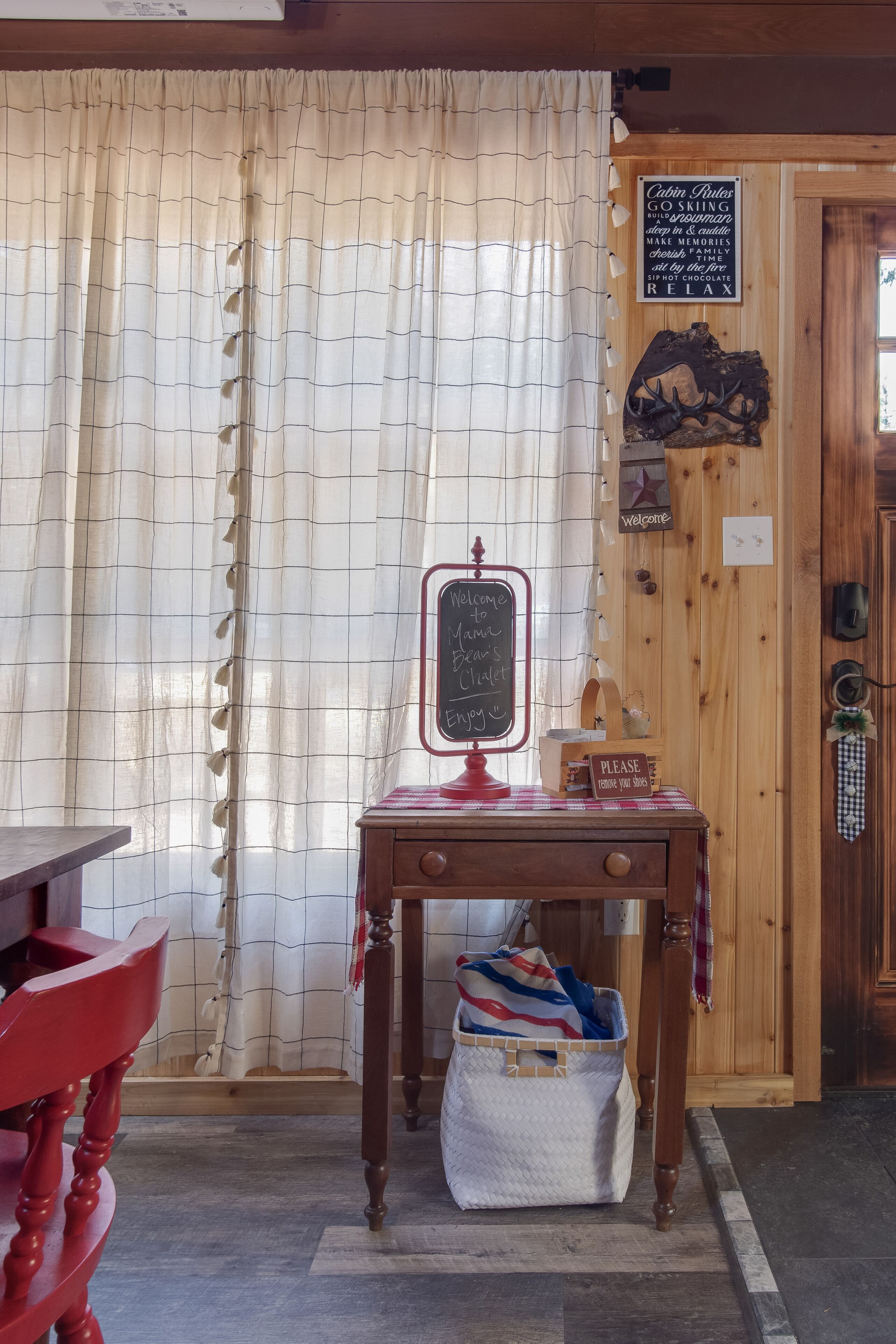 A cozy room with a wooden door, a chalkboard sign, and a table with a basket.