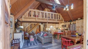 Un'ampia stanza in stile loft con soffitto alto, travi in legno, zona pranzo e angolo cottura.