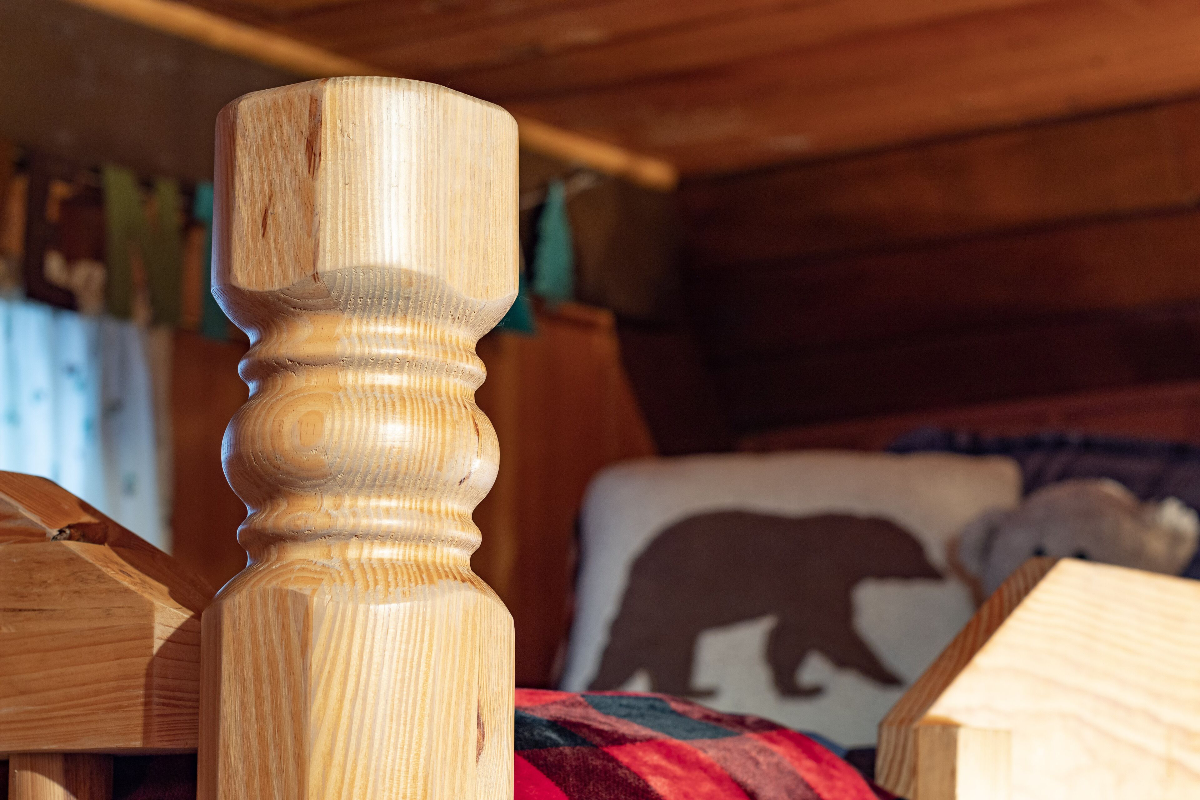 Una silla de madera con respaldo tallado en una habitación con paredes de madera y un cojín con motivos de oso.