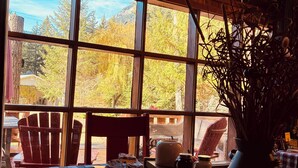 Un'accogliente sala da pranzo con tovaglia a quadri, sedie di legno e un'ampia finestra vista alberi e montagne.