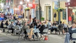 Ein Essbereich im Freien bei Nacht mit Tischen und Stühlen, umgeben von mehrstöckigen Gebäuden mit verschiedenen Geschäften.