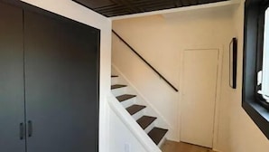 Eine Treppe mit Holzsitzen führt zu einer Tür, einem schwarzen Schrank und einer Deckenleuchte.