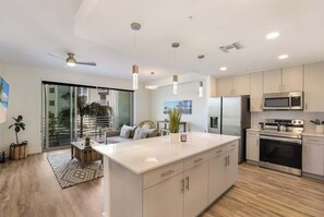 Cozinha moderna com ilha central, eletrodomésticos de aço inoxidável e porta de vidro deslizante para uma varanda.