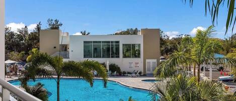 A pool area with a modern building, palm trees, and lounge chairs.